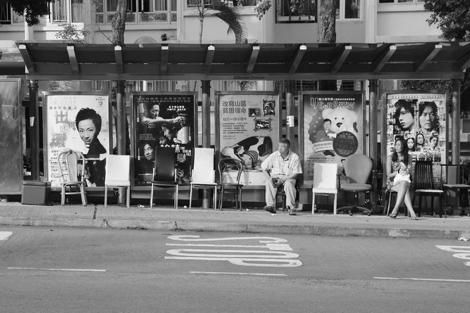 Man sitting at bus stop with a variety of indoor chairs lined up under the canopy.