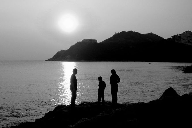 Silhouettes of three people on the shore of Stanley Bay with the sun setting behind them. 