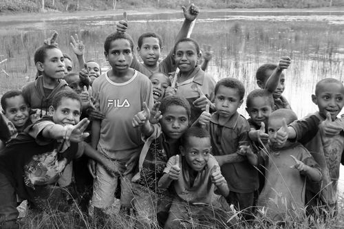 Children standing before a small pond giving the camera a thumbs-up.