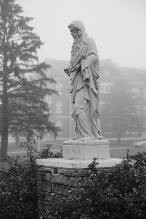 St. Paul statue with a dorm in the background obscured by fog. 