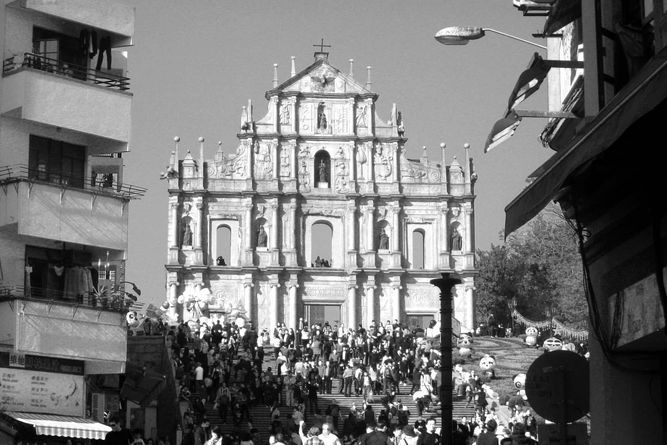 Front steps and facade of St. Paul's Cathedral in Macau surrounded by local buildings.