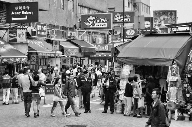 Entrance to Stanley Market with about 25 people walking in front of shops. 
