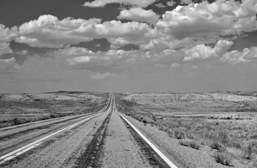 A view down the empty highway with fields and hills on either side.