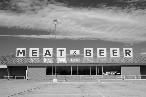 Local grocery store with a large sign on top of the building that says "Meat and Beer"