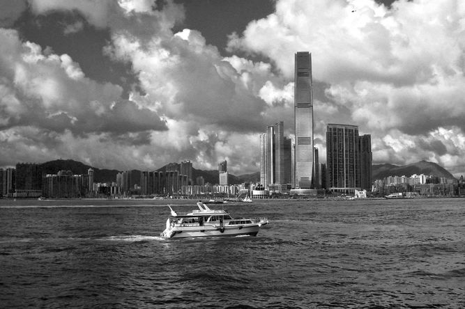 A junk boat sailing through Victoria Harbor, skyscrapers and residential buildings in the background.