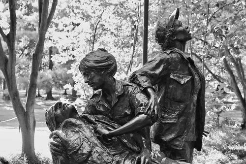 Bronze statue of two women attending a wounded soldier in front of a background of trees.