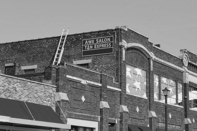 Brick buildings with Awe Salon painted on the side with an extention ladder leading from one roof to the next roof.