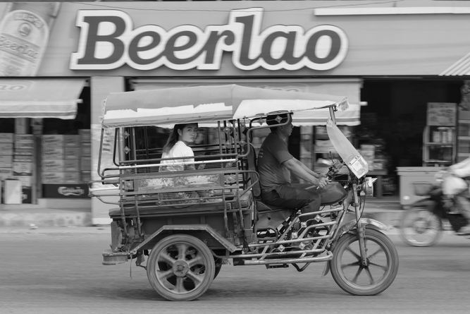 A woman riding in a Tuk Tuk, with a sign that says Beerlao in the background.