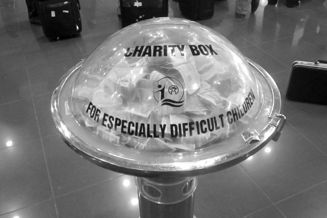 A clear plastic dome charity box labeled "For Especially Difficult Children" filled with paper money.