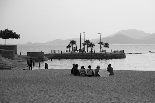 View of the bay from the beach with people sitting on the sand watching the water.