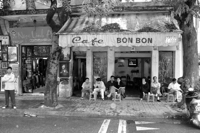 Little cafe on a street with patrons sitting outside on stools.
