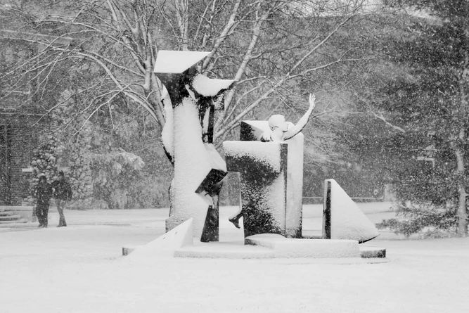 Snow falling on the quad with the Son of Man Be Free statue at the center.