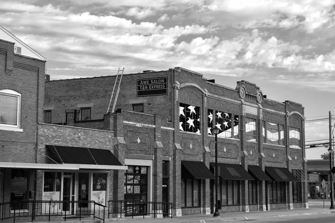Brick buildings with Awe Salon painted on the side with an extention ladder leading from one roof to the next roof.