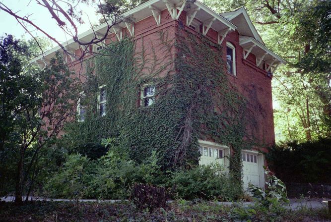 Two-story garage made from red brick and covered in vines.